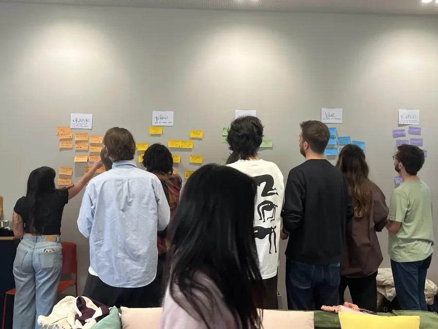 A team working a wall of sticky notes in person, clustering under colour-coded headings